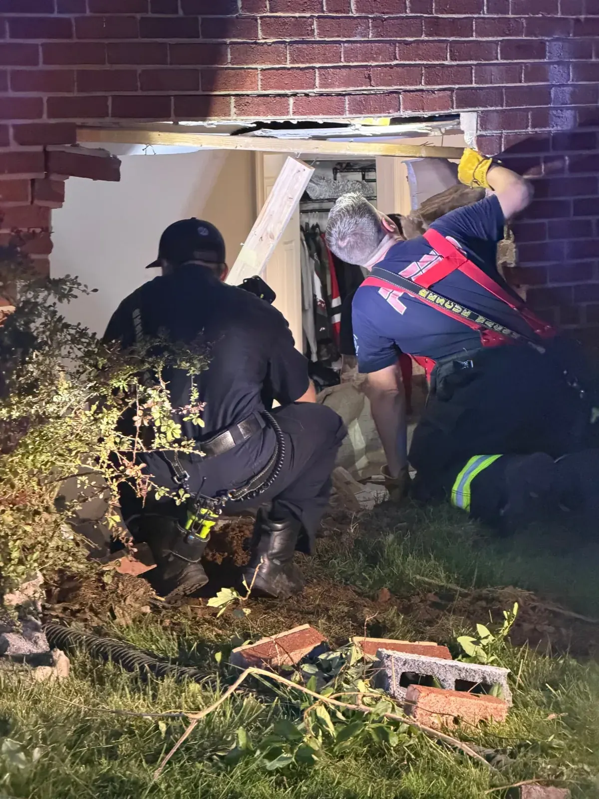 Fire rescue crew at a vehicle impact opening in the brick wall of a home at night on an EMC project