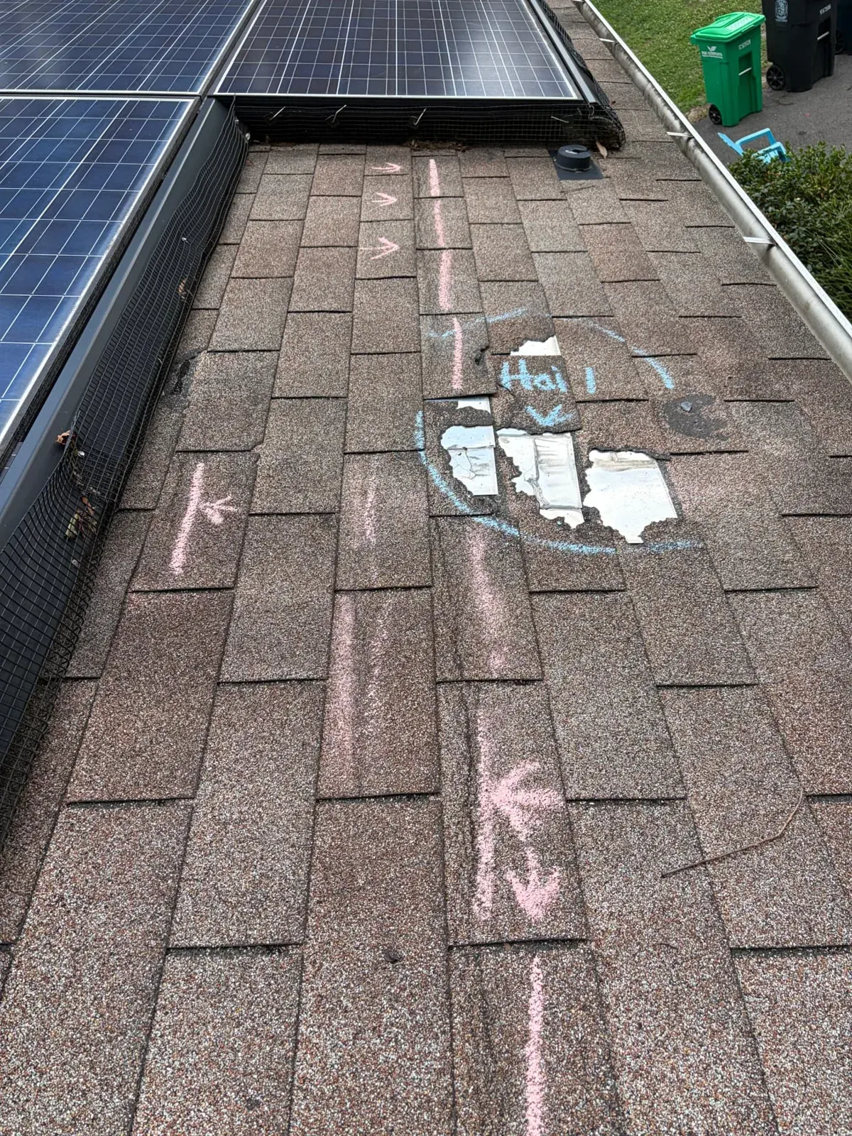 Asphalt shingle roof with hail damage and missing tabs marked in chalk beside solar panels during an EMC hail inspection