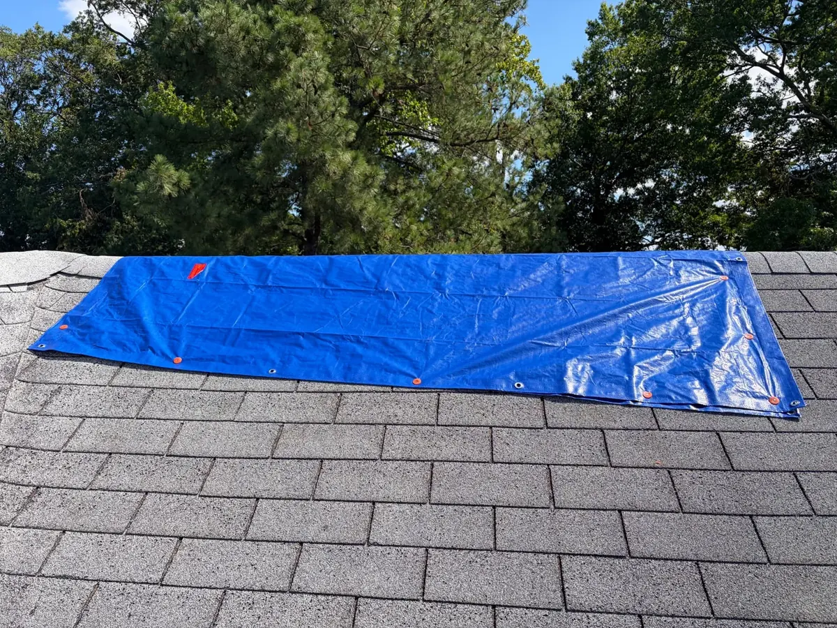 Blue emergency roof tarp secured across an asphalt-shingle slope on an EMC project