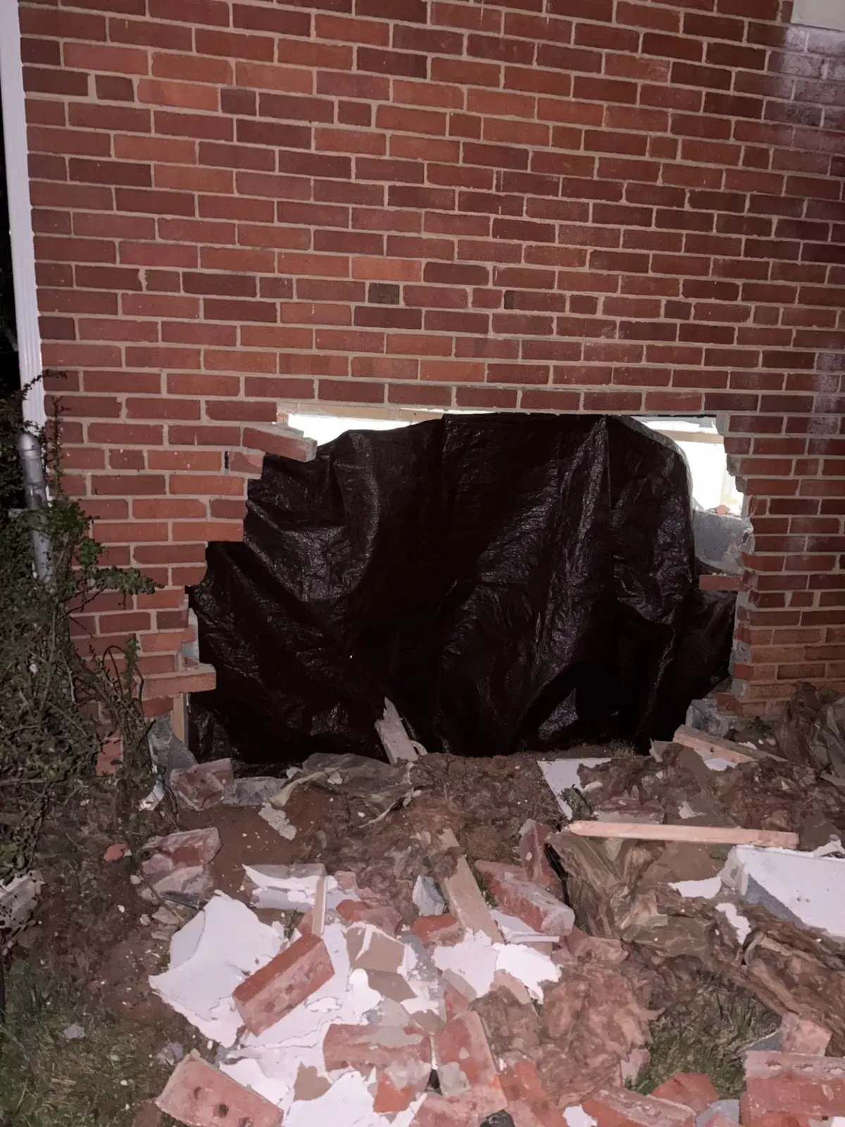 Vehicle impact hole in a brick home wall covered with black poly sheeting by EMC Response at night