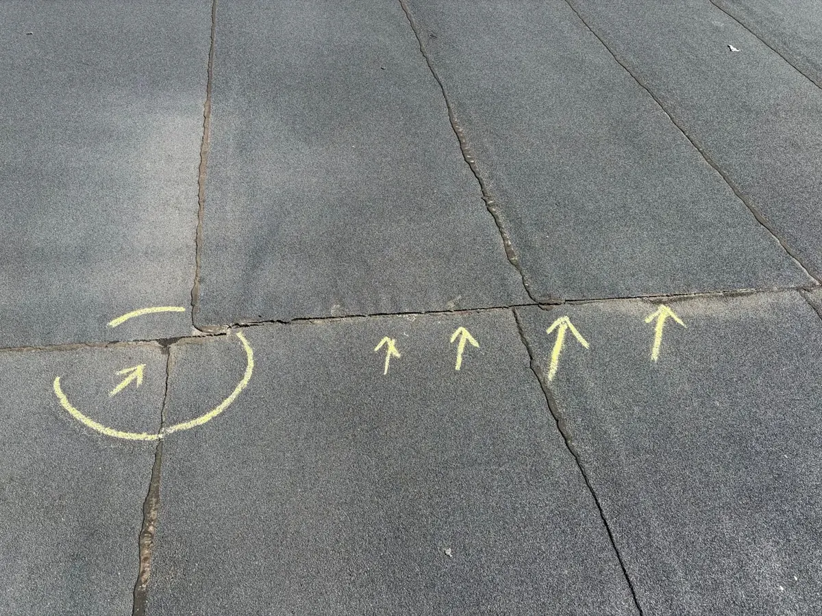 Separated seams on a flat modified-bitumen roof marked with yellow chalk arrows during an EMC roof repair inspection